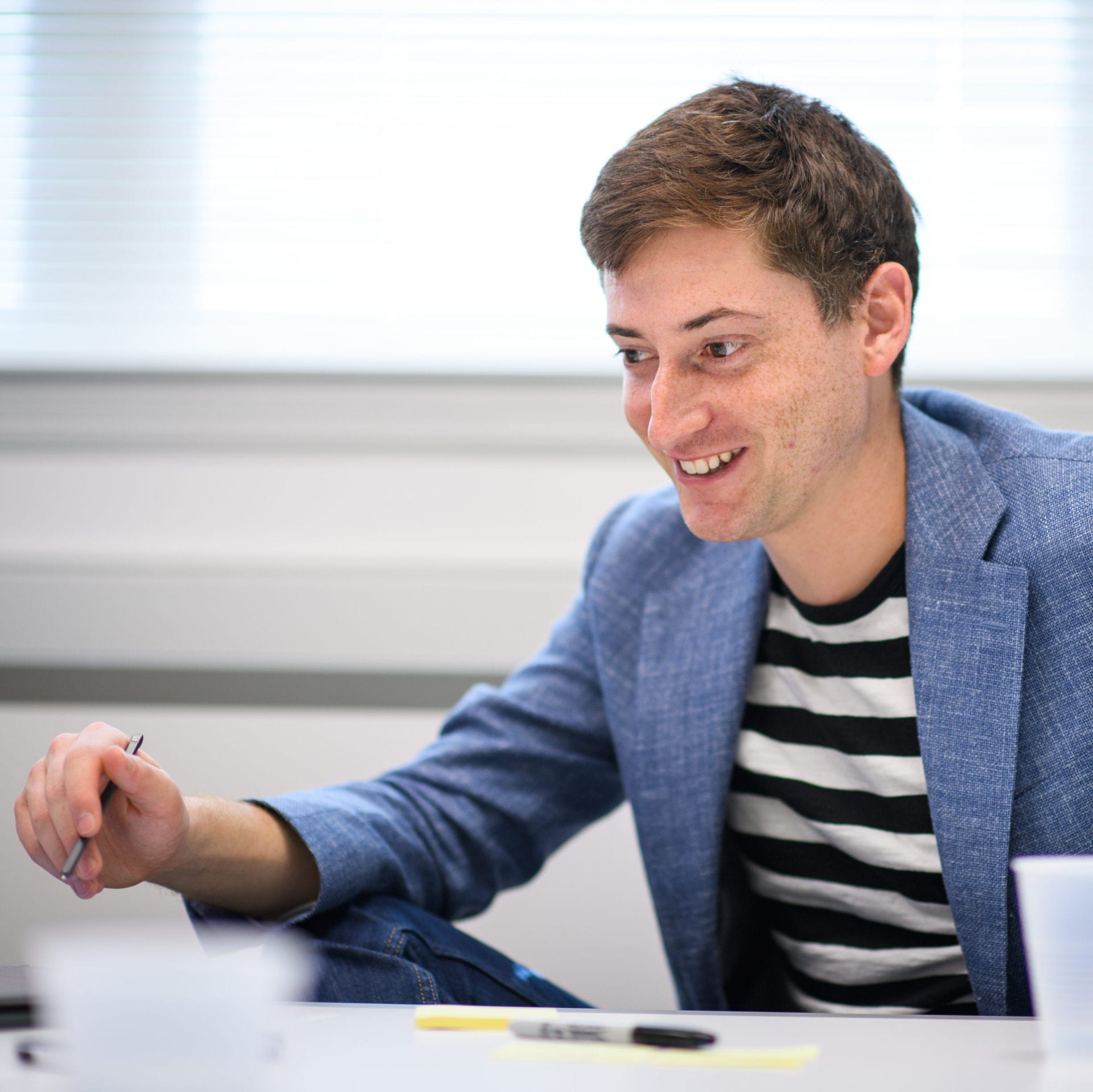 Rafe Steinhauer, M.Ed./M.B.A., Tulane Visiting Assistant Professor of Design Thinking, smiles while holding a marker near a table.