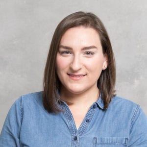 Shaina Spector smiling wearing a denim button-up shirt.