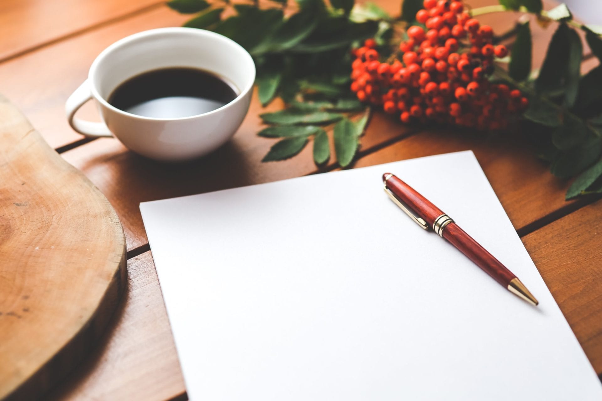 A table with a coffee mug, blank paper, pen, and flowers.
