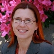 Nora Ellertsen smiling wearing a gray shirt in front of pink flowers.
