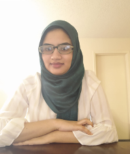 Tahmeena-Fnu A person smiling wearing a white shirt and glasses in front of a white wall.